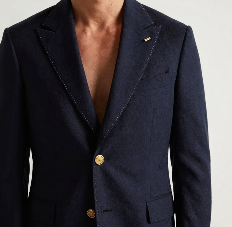 Vertical portrait of a gentleman wearing a perfectly draped bespoke navy blazer, hand-stitched gold lapel buttonhole detail, warm side lighting, clean white background.
