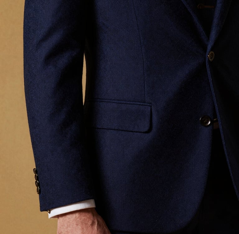 High-fashion editorial crop of a man in a sharp navy blue wool suit, dramatic side lighting, rich fabric texture visible, gold cufflink detail.