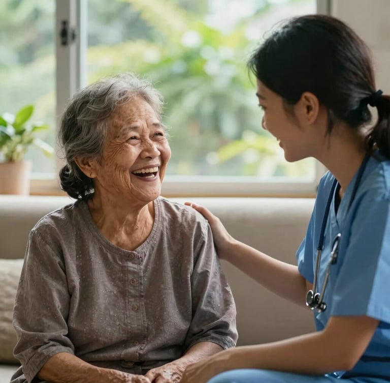 Candid eye-level medium shot of an elderly Malaysian grandmother laughing warmly with a young female caregiver in a sunlit living room, soft morning daylight, natural green foliage visible outside the window.