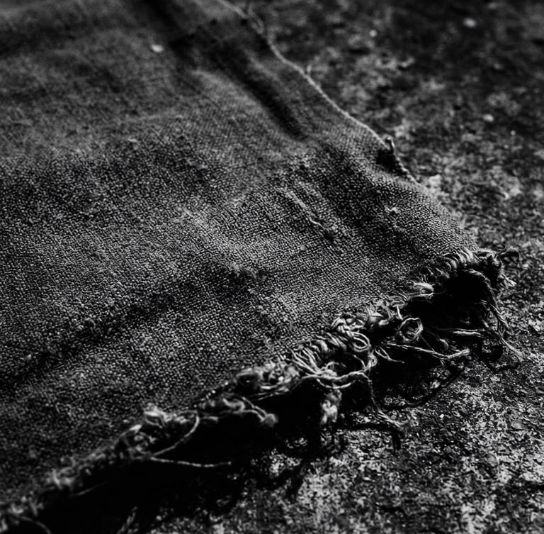 moody monochrome photography of a heavy cotton fabric texture with raw edges, harsh shadows, concrete background, 35mm film style