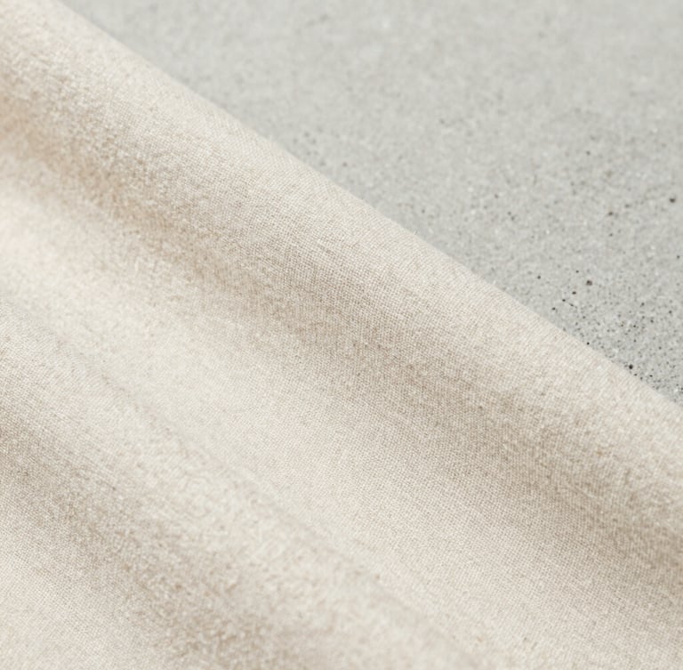 Close-up macro shot of the weave of a high-grammage organic cotton fabric, showing fine texture and natural fibers, under soft natural daylight, minimalist editorial product photography, sharp focus, neutral concrete background, 35mm