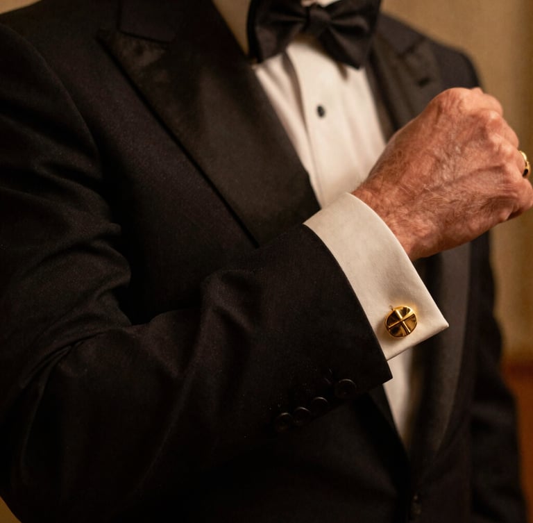 Close-up of a perfectly tailored bespoke tuxedo sleeve and gold cufflink, warm low-key atmospheric lighting, deep shadows, luxury Mayfair aesthetic