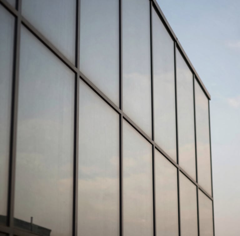 Macro shot of architectural glass panels reflecting neutral daylight and a crisp blue sky.