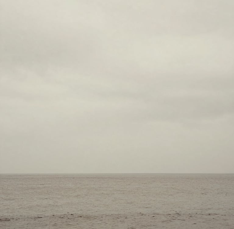 Calm sea under a heavy overcast sky, horizon line barely visible, minimalist fine art photography, desaturated earth tones