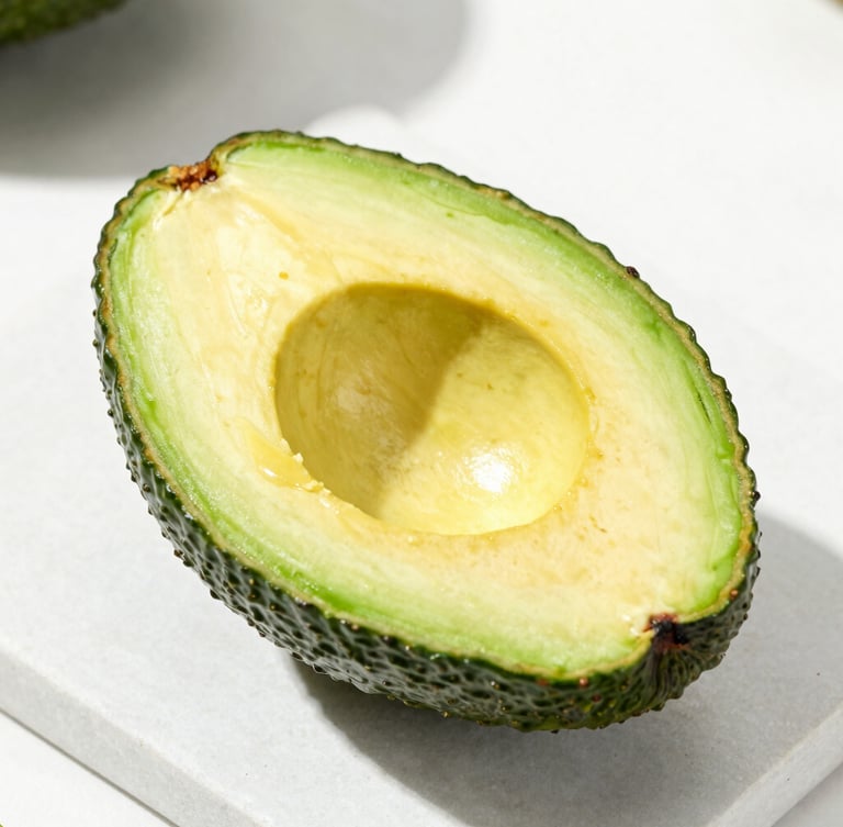 A pristine sliced Hass avocado showing its rich buttery texture and green skin, resting on a clean white stone surface, bright natural daylight, 50mm