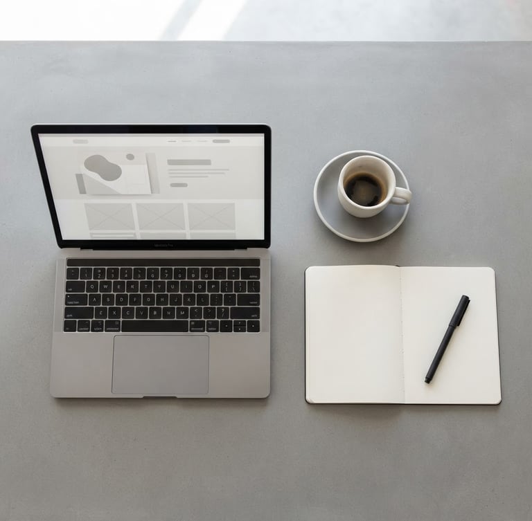 A minimalist overhead flat lay of a clean workspace with a laptop displaying a modern website mockup, a notebook, and a ceramic coffee cup on a neutral grey table, bright soft studio light.