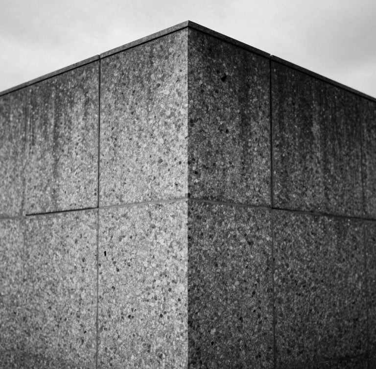 Straight-on architectural elevation of a monolithic granite wall, sharp joint lines, raking side-light highlighting the hand-chiseled texture, overcast daylight, desaturated slate tones.