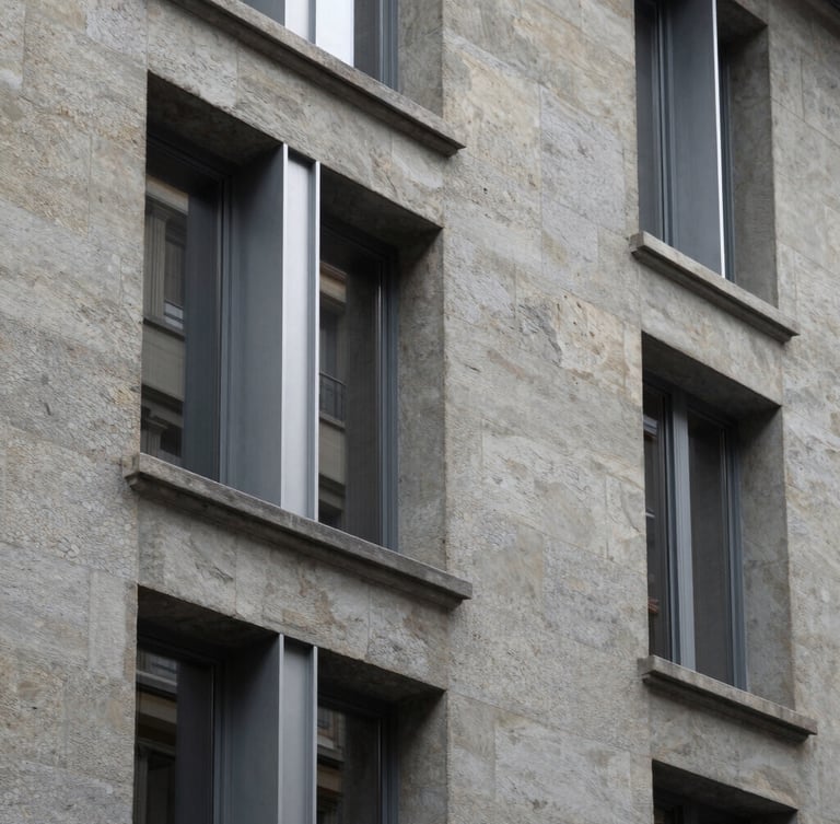 Abstract architectural detail of a renovated historic stone facade in Lausanne, showing the contrast between clean modern metal window frames and textured grey stone, soft northern light.