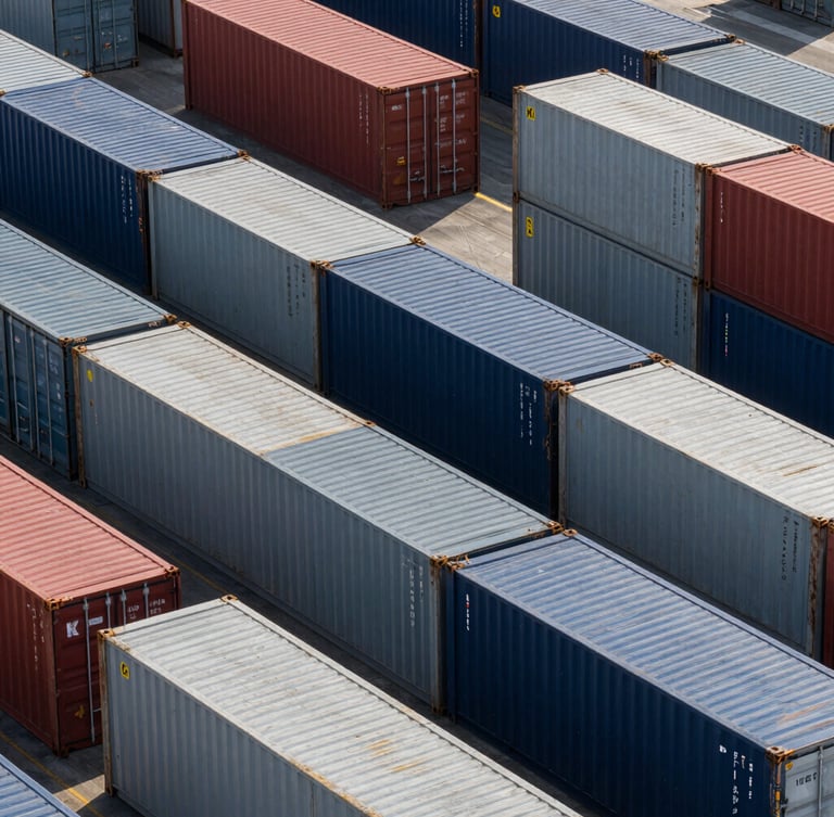 Overhead geometric pattern of multi-colored shipping containers stacked precisely in an automated terminal, sharp morning light, high contrast.