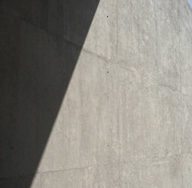 Close-up of a textured concrete wall with sharp geometric shadows from direct sunlight, minimalist architectural aesthetic, desaturated neutral tones, 35mm lens.