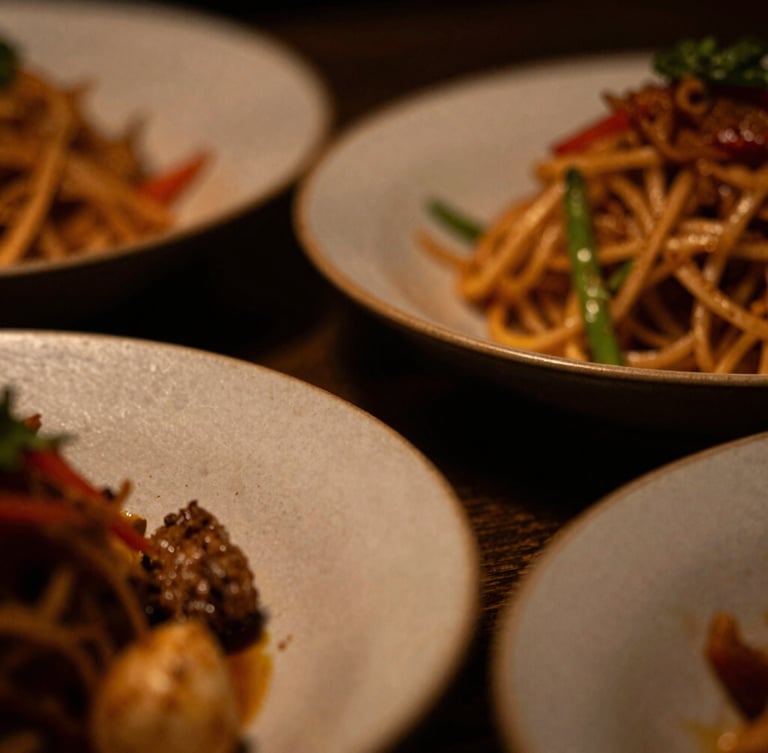 Close-up macro shot of textured ceramic plates with a vibrant Asian fusion dish, dramatic low-key side lighting, warm amber tones, extreme shallow depth of field, 35mm