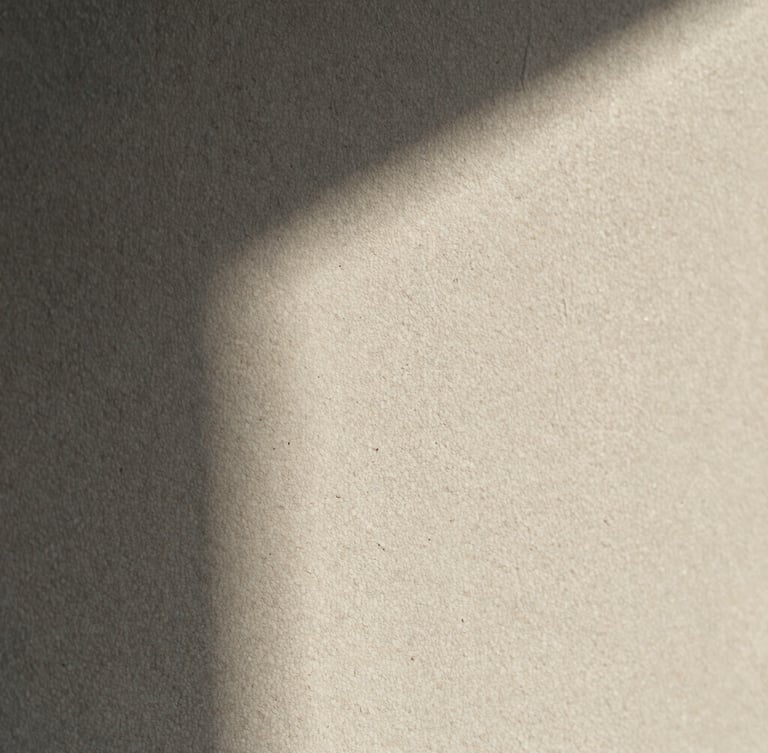 Extreme close-up of a textured plaster wall showing fine mineral grains under soft morning light, architectural shadow casting across the surface.
