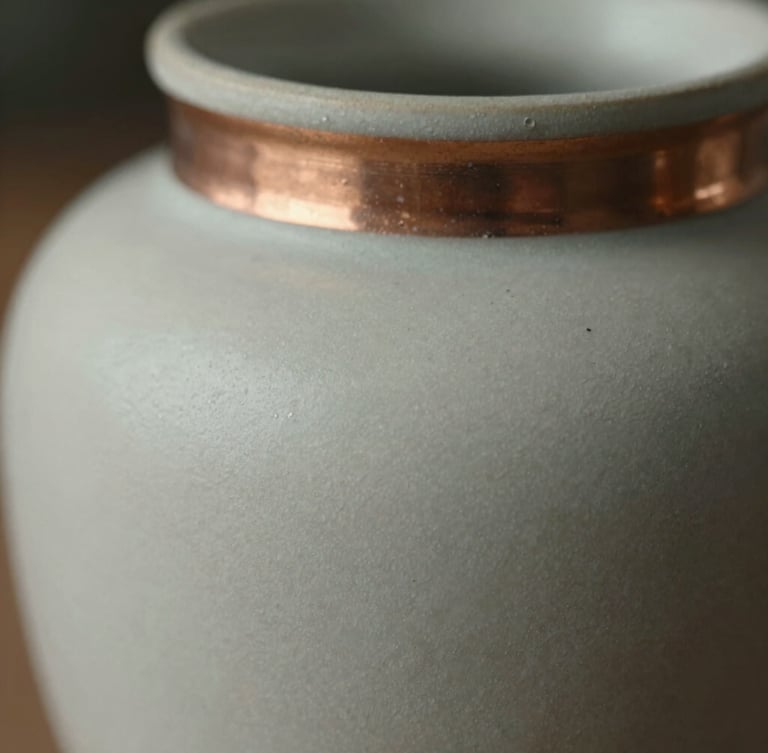 Close-up macro shot of matte ceramic texture and brushed-copper accent details, soft directional natural light.