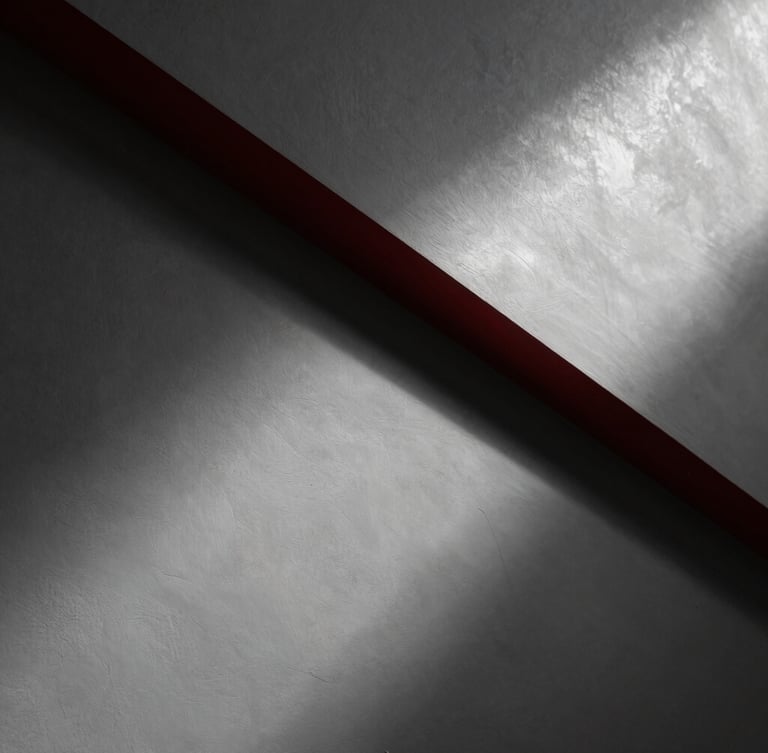 Dramatic low-angle raking light sweeping across a freshly sanded, perfectly flat plaster wall, showing ultra-smooth texture and clean geometric lines, architectural photography