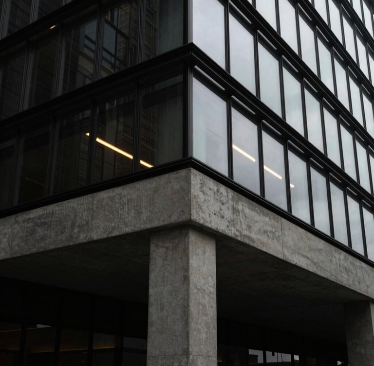 A sharp architectural close-up of a modern concrete foundation meeting a glass facade, low-key dramatic lighting with a single gold light trail reflecting on the glass.