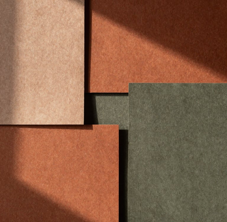 A tall portrait shot of textured handmade paper swatches in warm terracotta and muted olive tones, soft directional afternoon light casting deep shadows.