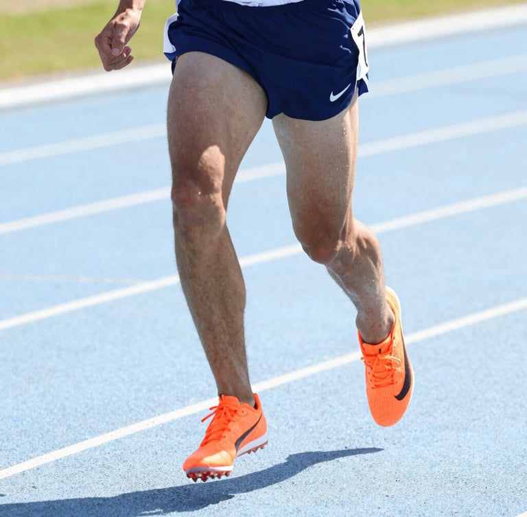 Bright high-key athletic photography, close-up of a focused athlete sprinting on a track in crisp natural daylight, vibrant orange details on shoes, sharp action freeze-frame, 35mm
