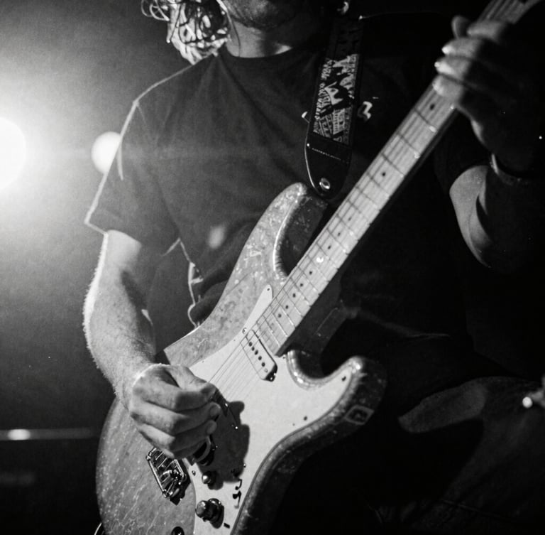 Extreme close-up, low-angle, high-contrast black and white shot of a guitarist's hand shredding on a battered electric guitar, stage lights creating lens flares, motion blur, 35mm film grain, bleeding right.
