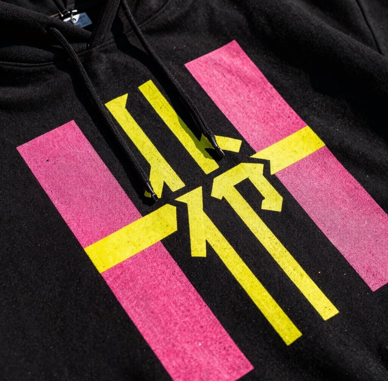 Extreme close-up of a high-contrast neon graphic print on a black streetwear hoodie, vibrant pink and yellow ink texture visible, flash photography