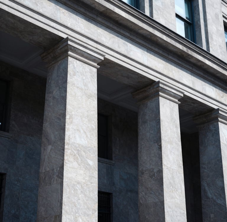 Low angle architectural view of a classic bank building facade with stone pillars, cool-toned daylight, sharp focus, deep navy shadows.
