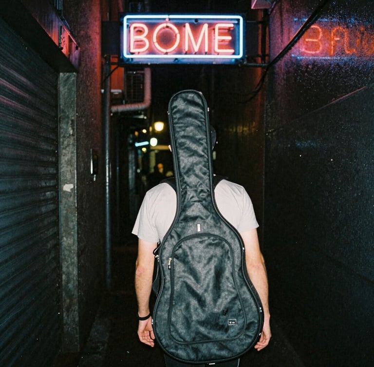 Candid street-style shot of a musician carrying a guitar case down a dark, wet alleyway illuminated by a flickering neon sign.