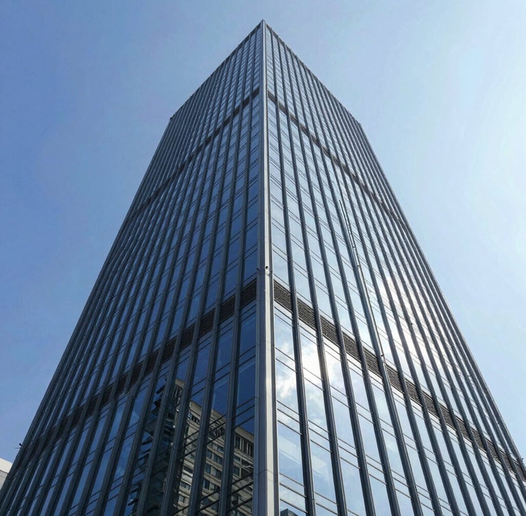 Low-angle architectural shot of a towering commercial glass facade reflecting a bright blue sky, crisp daylight, sharp geometric lines