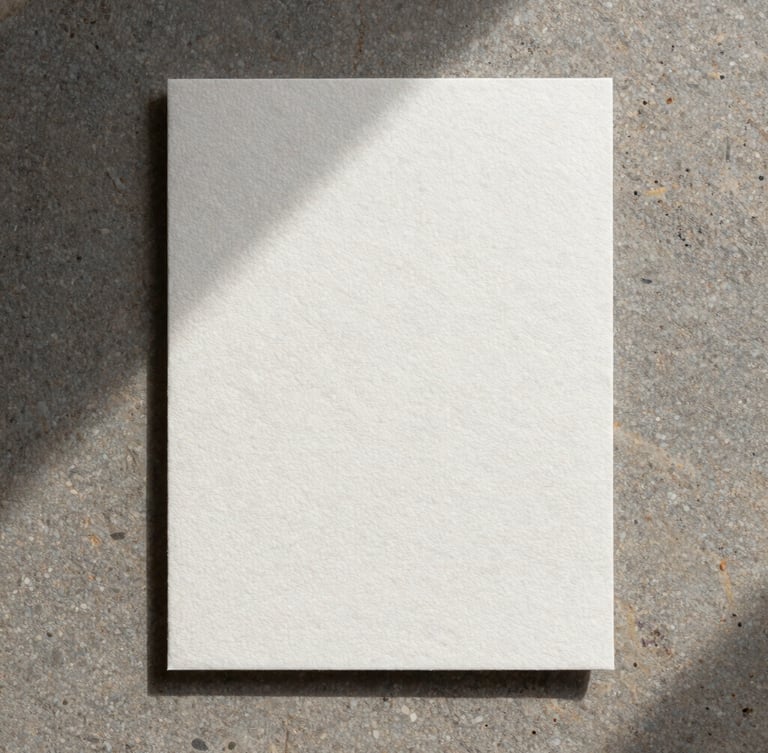 A top-down flat-lay of heavy embossed cotton paper stationery on a raw stone slab, soft diffused natural light, long gentle shadows.