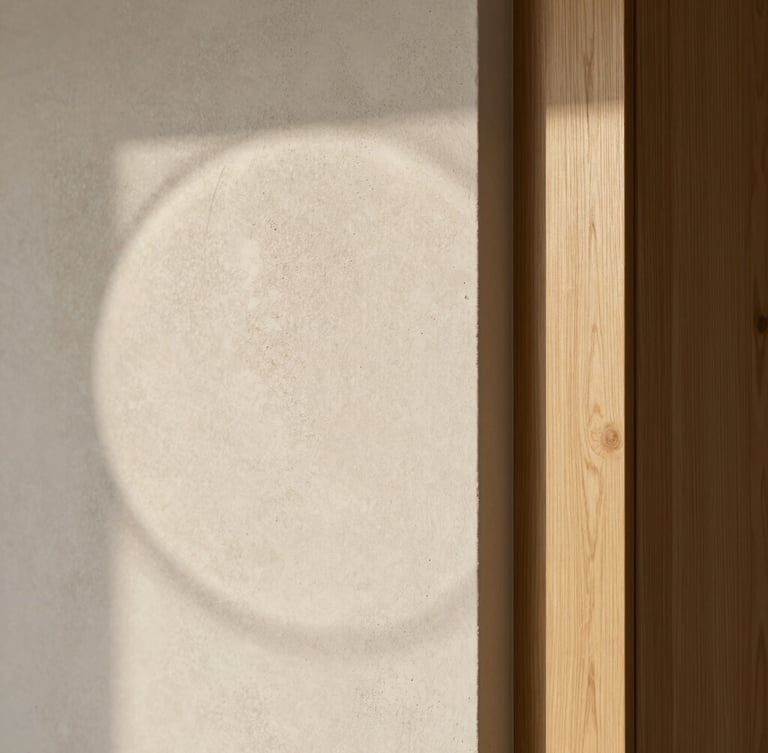 Soft natural daylight casting a subtle circular shadow on a textured microcement wall, intersecting with a flawless, sharp light oak joinery corner. Minimalist, architectural, serene composition with generous negative space, high-end detail.