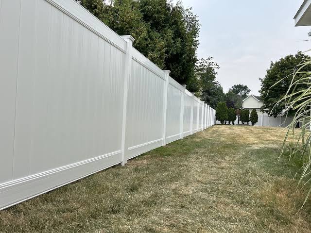 White vinyl privacy fence installed along a backyard lawn for residential security.