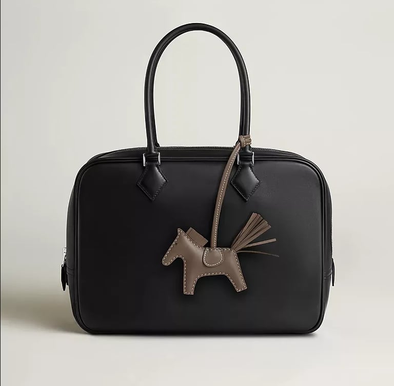 Hermes Elegant black leather handbag with a designer horse charm accessory and double top handles.
