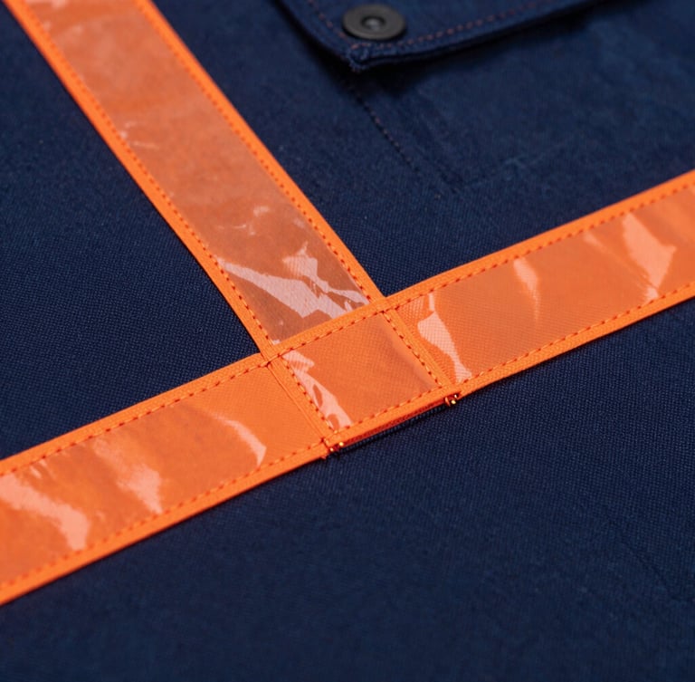 Macro shot of heavy-duty triple-stitching on deep navy workwear fabric with orange reflective safety tape, crisp workshop lighting, industrial product photography, 50mm lens