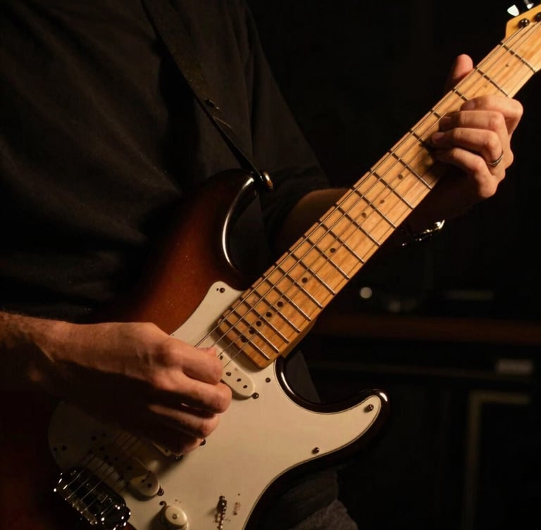 Close-up of hands navigating the fretboard of an electric guitar, low-key dramatic studio lighting, warm amber backlights, deep shadows