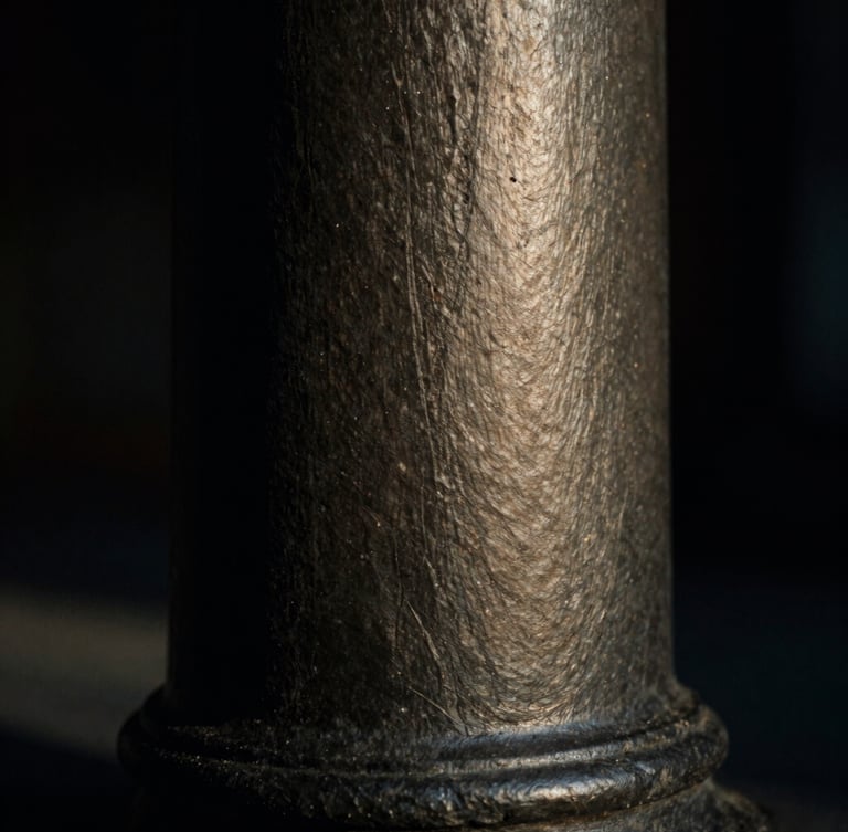 Macro close-up of a dark slate architectural column in low-key dramatic chiaroscuro lighting, brushed metal texture, 35mm film.