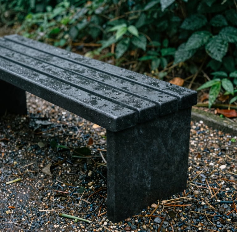 Close-up of a freestanding storage bench made of dense dark resin, wet from morning dew, placed on a gravel path, 35mm