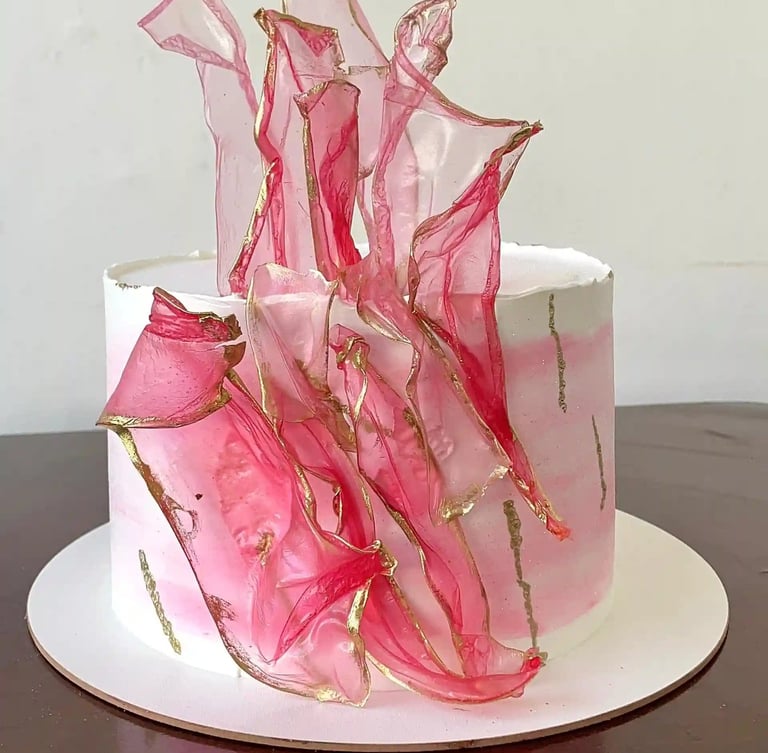 Bolo decorado com detalhes em rosa e dourado, apresentando decoração com açúcar em forma de fitas. I