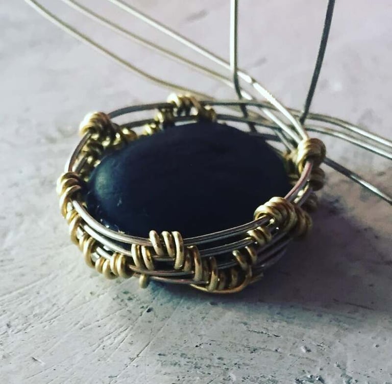 Colgante de joyería hecho a mano con alambre engarzado, que presenta una piedra oscura engastada