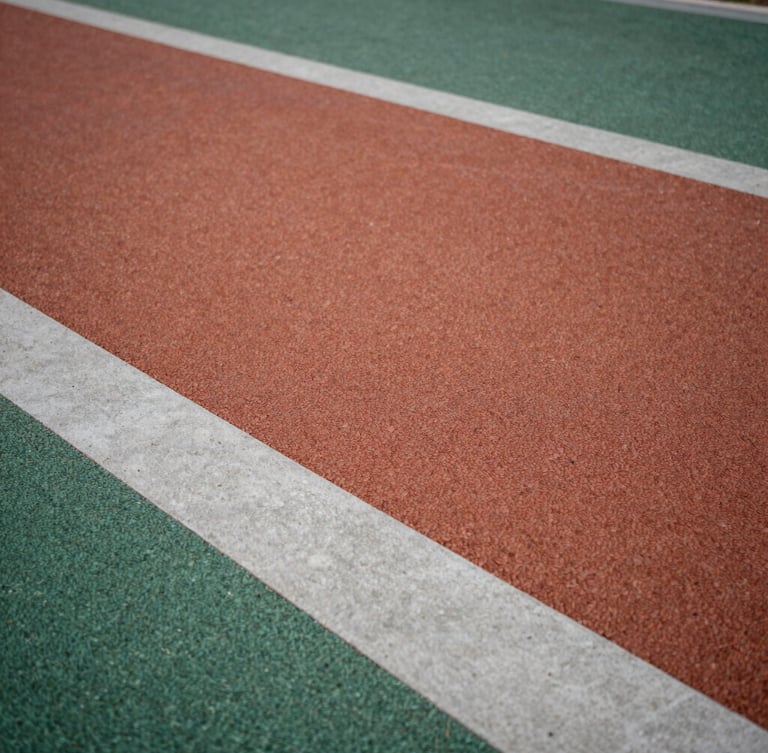 Low-angle architectural shot of a modern playground floor, textured terracotta and forest green rubber tiles meeting clean concrete edges under soft overcast daylight, macro texture visible.