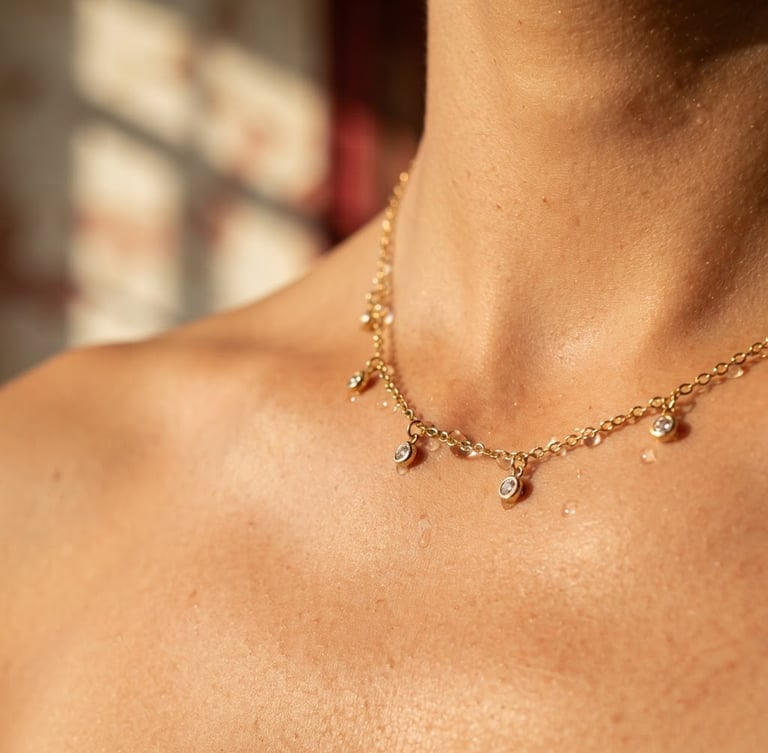 Macro close-up of a delicate gold-plated stainless steel necklace resting on warm skin, water droplets glistening on the metal, soft golden hour sunlight, architectural shadows