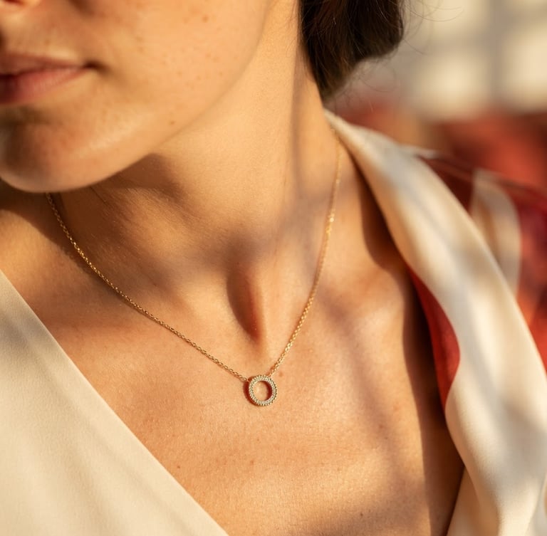 Macro close-up of a delicate stainless steel gold-plated necklace resting on a woman's collarbone, warm direct sunlight casting soft architectural shadows, cream background, high-end editorial photography.