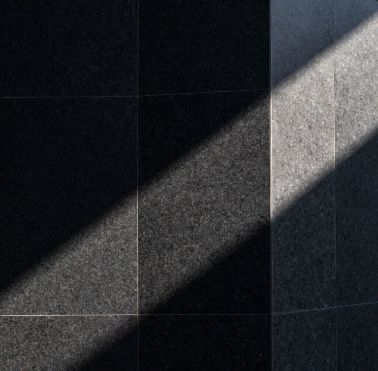 Abstract architectural crop of a monolithic black granite structure, sharp sunlight cutting across raw stone, deep shadows, high-contrast minimalist composition.
