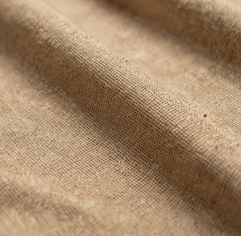 Macro photograph of a heavy-weave Belgian linen, warm sand color, dramatic side light emphasizing the thick natural slub and structural texture