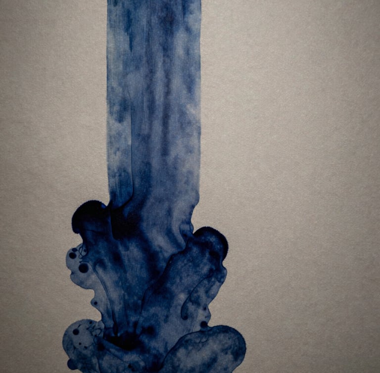 Macro architectural shot of deep indigo ink bleeding into heavy, warm stone-gray cotton paper, soft directional side-lighting casting subtle shadows, gallery exhibition feel.