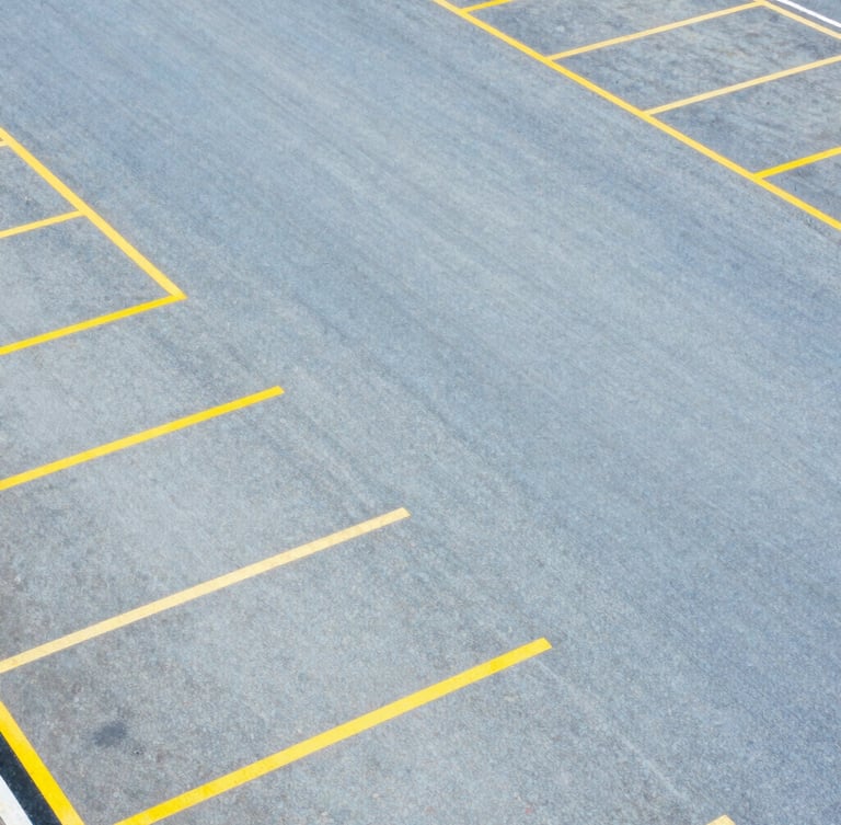 Overhead aerial view of an organized surface parking lot with clean yellow painted lines, sharp geometric layout, high contrast, bright daylight.