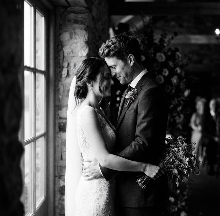 High-contrast black and white wedding portrait, a quiet moment between a couple under dramatic window light, editorial 35mm film look, rich shadows