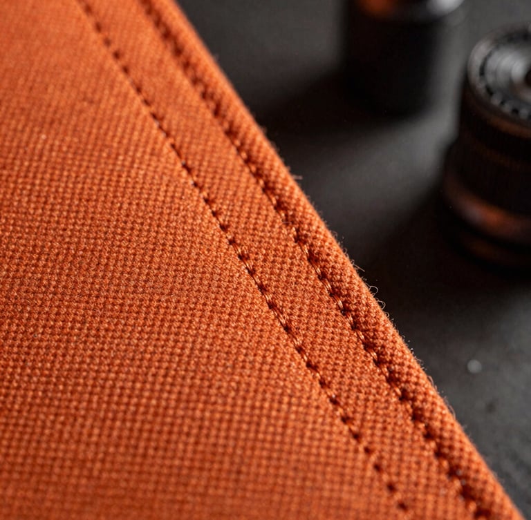 Macro shot of heavy-duty triple-stitched seams on high-denier orange canvas, dramatic cold workshop lighting with steel dust particles in the air