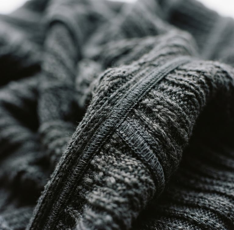 Extreme close-up of charcoal heavy-gauge technical knit fabric in motion, soft overcast window light, showing architectural drape and sharp seam details, 35mm