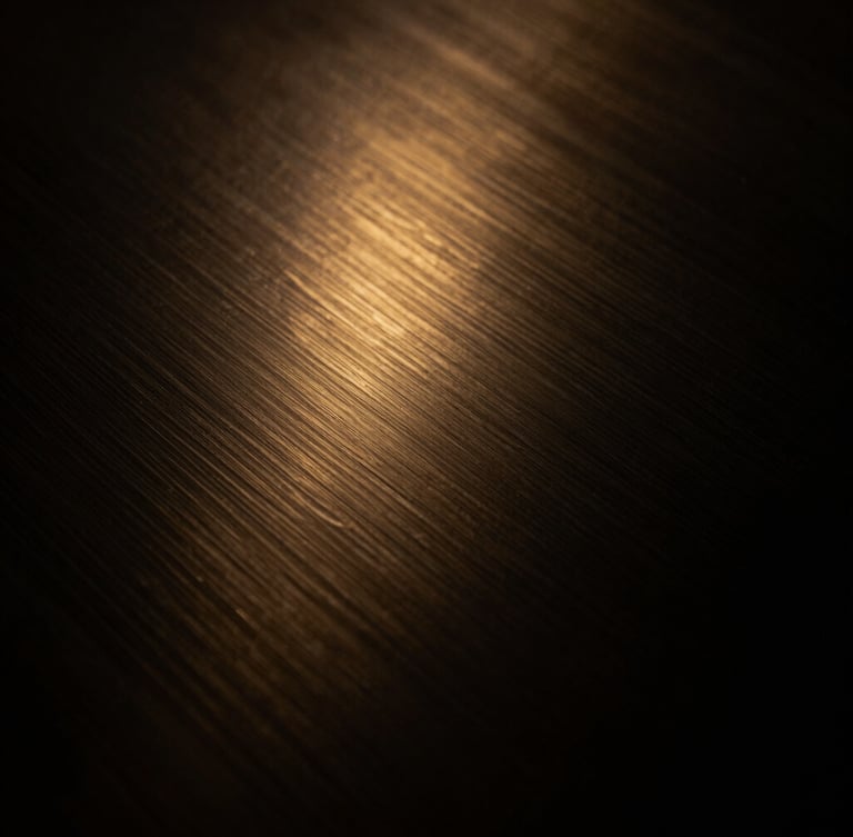 Close-up of a dark steel and brushed gold texture, low-key lighting, warm golden-hour accents, abstract and sophisticated.
