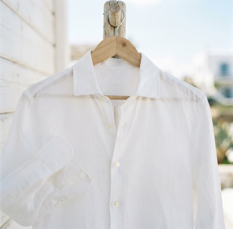 Close-up of a crisp white linen shirt on a natural wooden hanger, bright high-key coastal daylight, shallow depth of field, 35mm