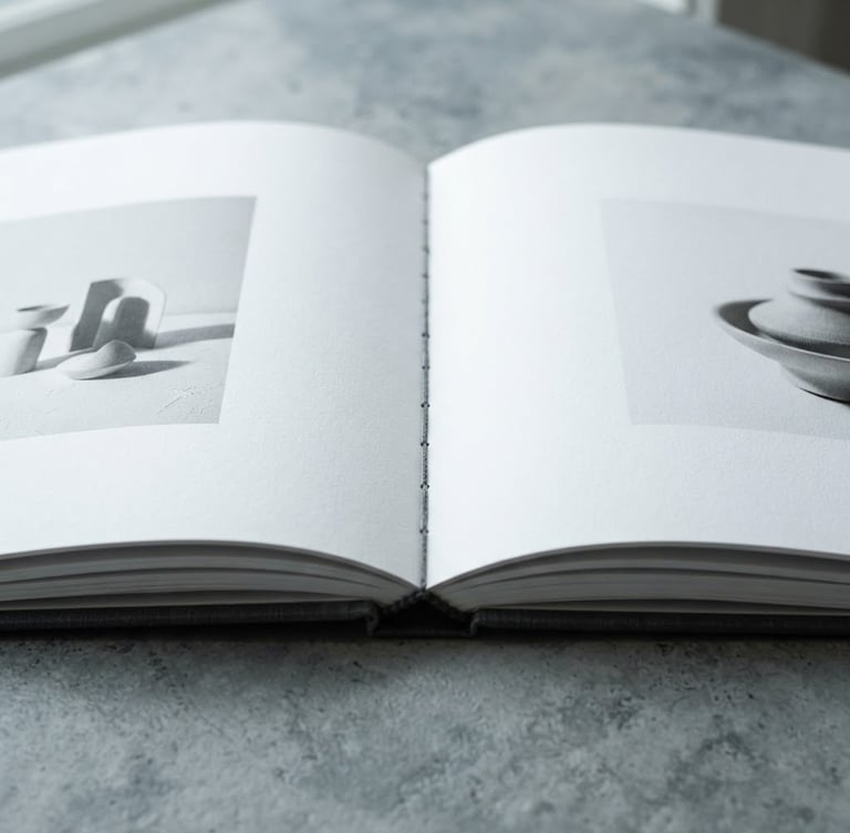 Minimalist editorial photography of a beautifully bound catalog open on a table, crisp daylight, cool slate and stark white tones, macro detail, 50mm