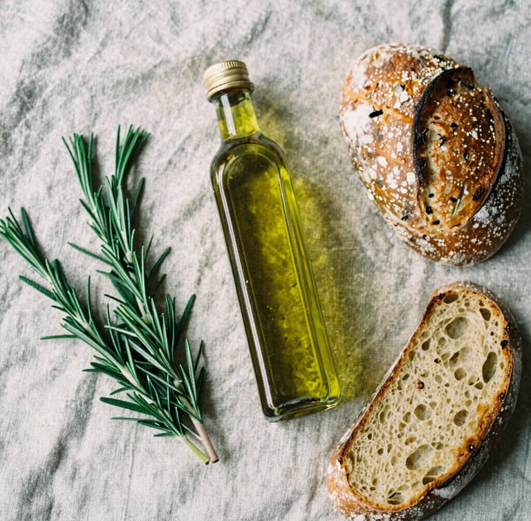 Overhead table spread of Greek olive oil, raw rosemary, and sourdough bread on a rustic linen cloth, soft natural side-light, rich crimson tones, 35mm film